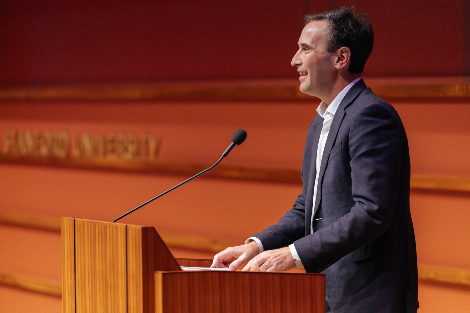 President Levin in suit smiling while speaking at podium.