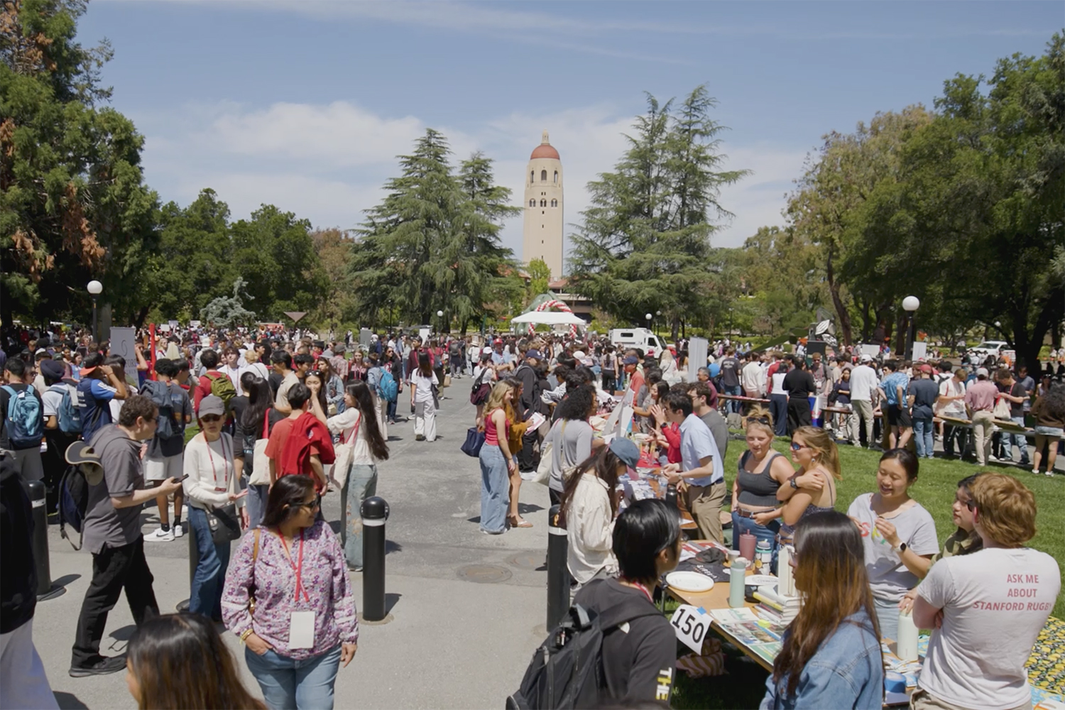 Open video Large outdoor campus event with crowds gathered near tables and tents, Hoover Tower visible in the background. in a modal