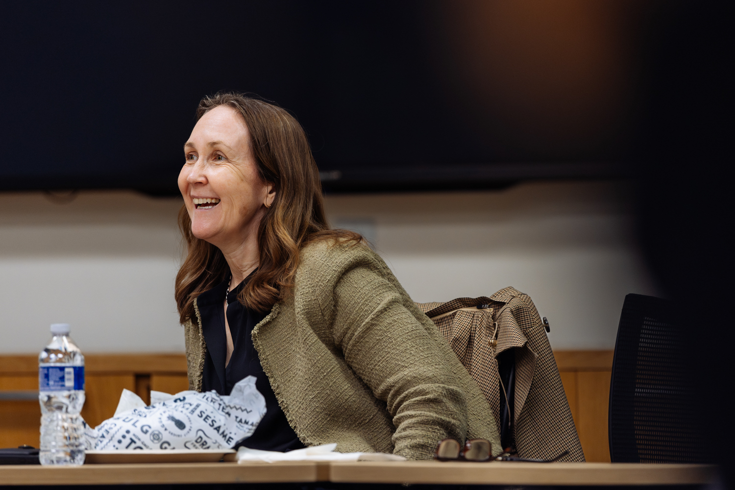 Jenny Martinez seated at a table with a water bottle and food, engaged in a discussion.