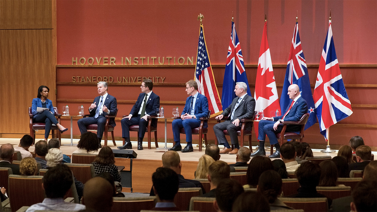 A panel discussion at Stanford’s Hoover Institution with speakers seated in front of various national flags and an audience listening attentively.