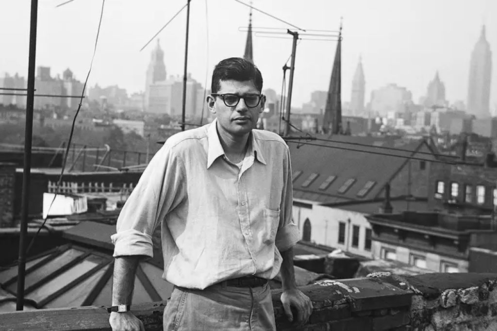 Young Allen Ginsberg stands on a rooftop with a skyline view of buildings, including the Empire State Building