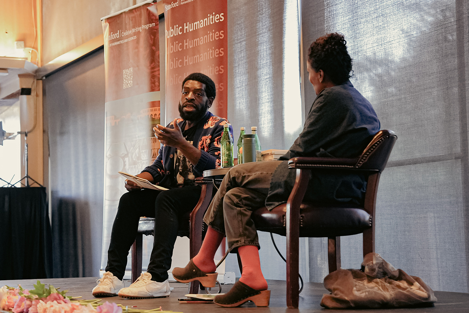 Hanif Abdurraqib on stage during a discussion, surrounded by promotional banners for Public Humanities at Stanford University.