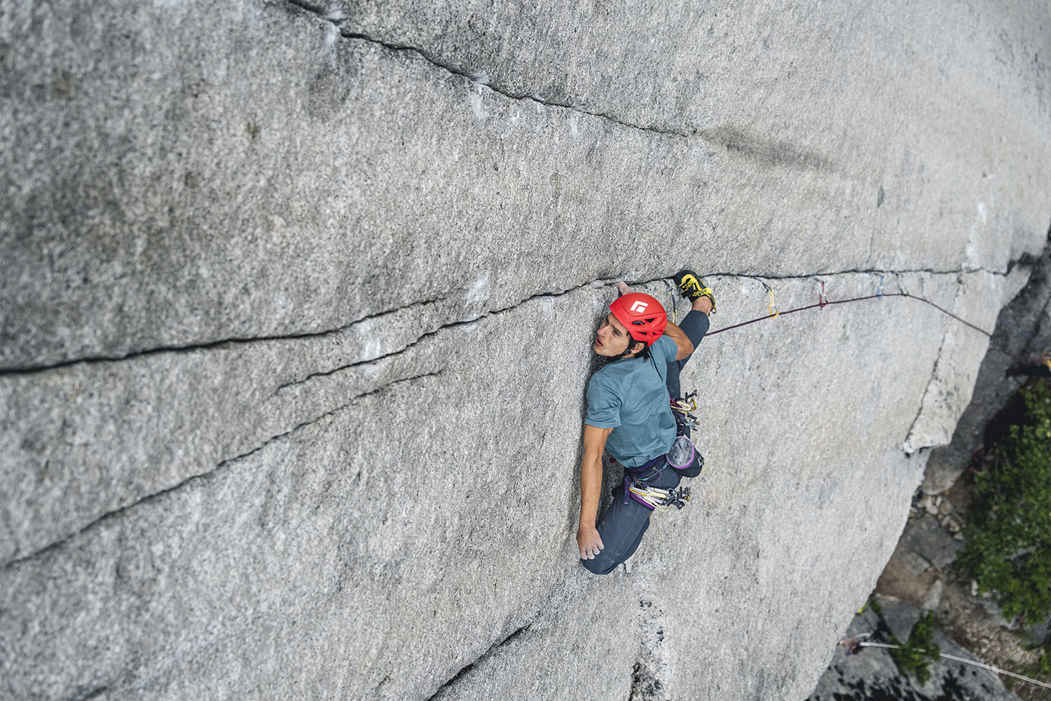 Climber Connor Herson ascends a steep rock face, wearing a helmet and harness, with climbing gear and ropes visible.