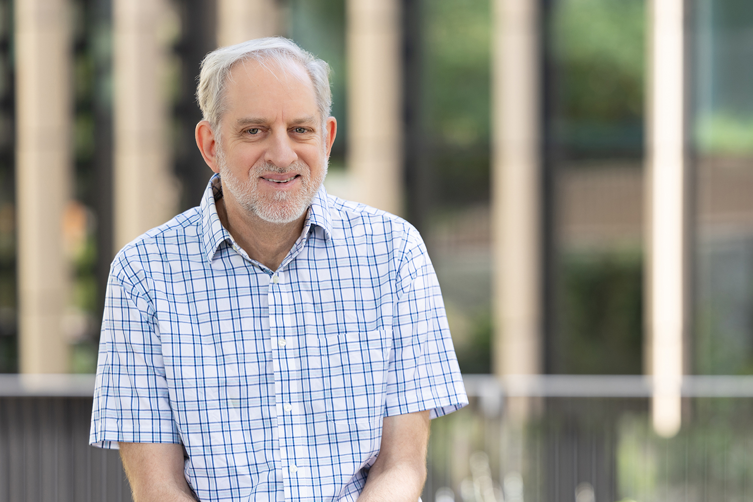 Davies with gray hair and short beard wearing a blue checkered shirt smiling outdoors.