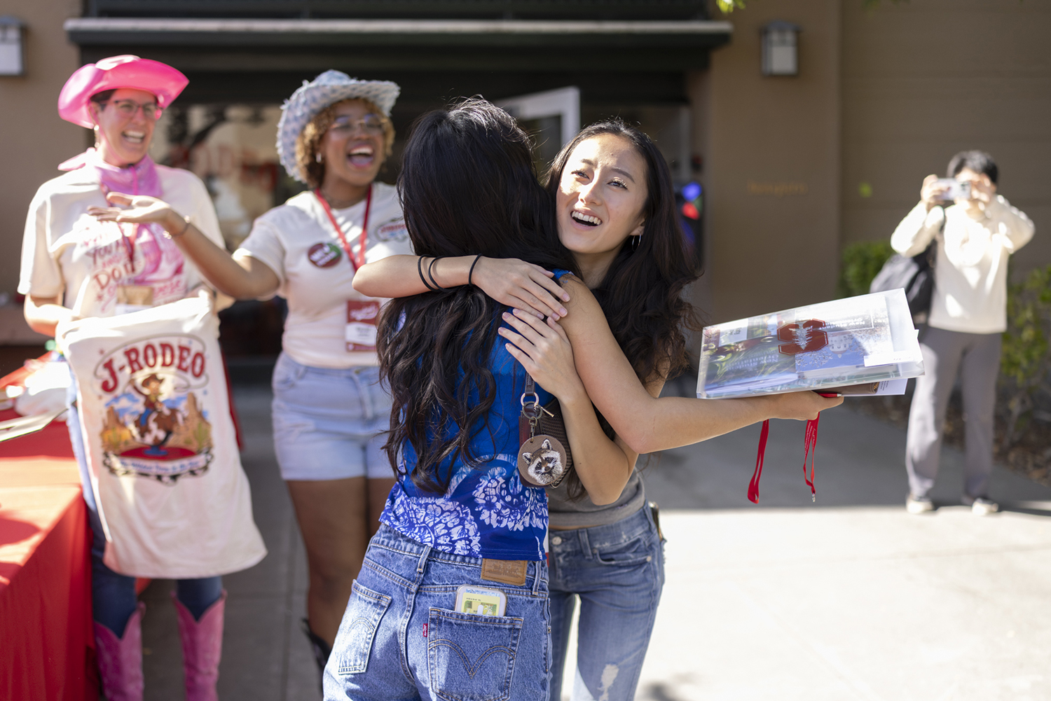 Two students hug and celebrate outside a residence hall while volunteers cheer nearby during Move-in Day.