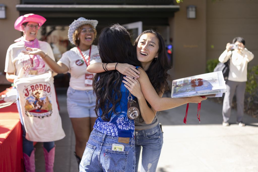 Two students hug and celebrate outside a residence hall while volunteers cheer nearby during Move-in Day.