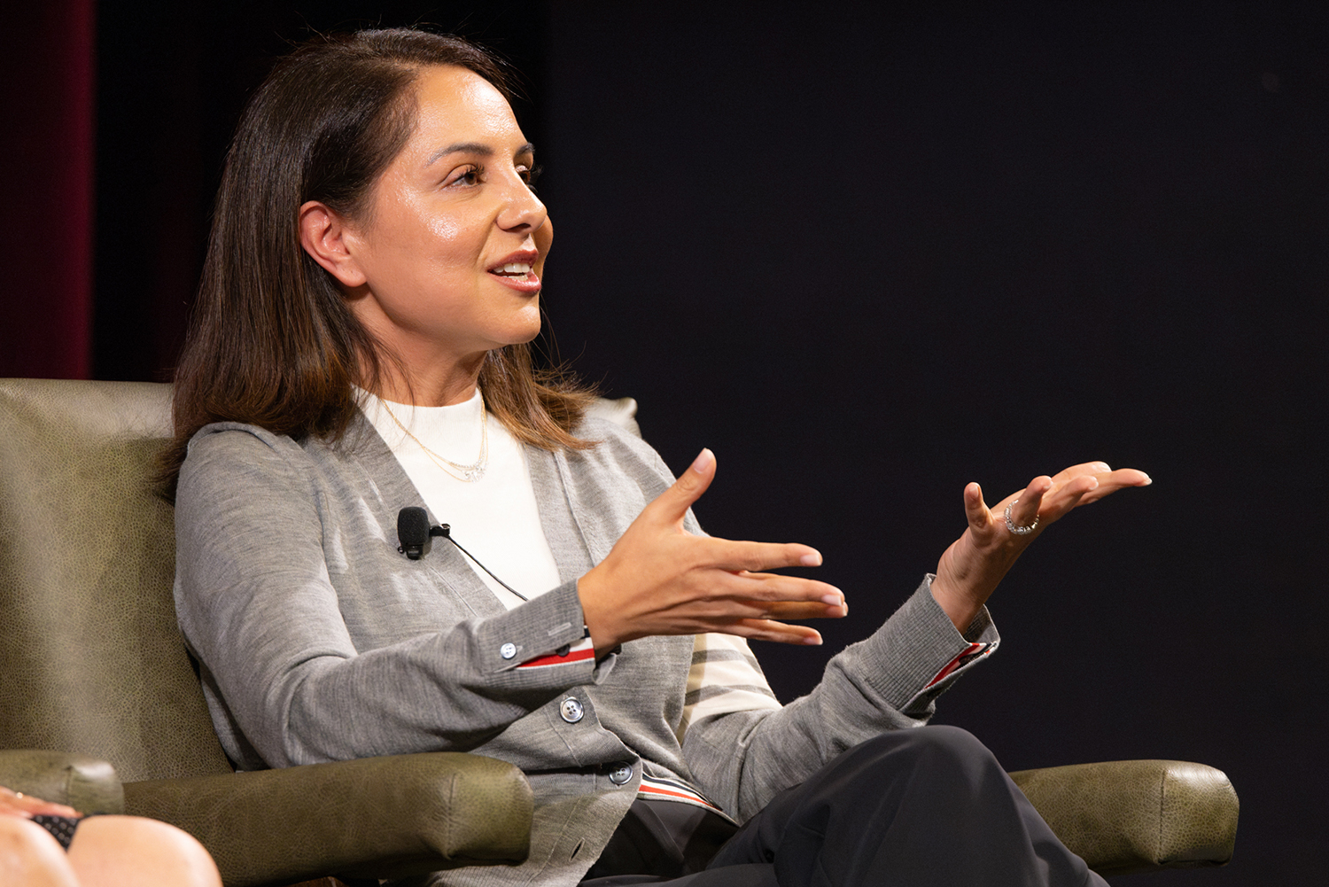 Lily Sarafan gestures and speaks to an audience while sitting in an armchair on stage during a panel event.