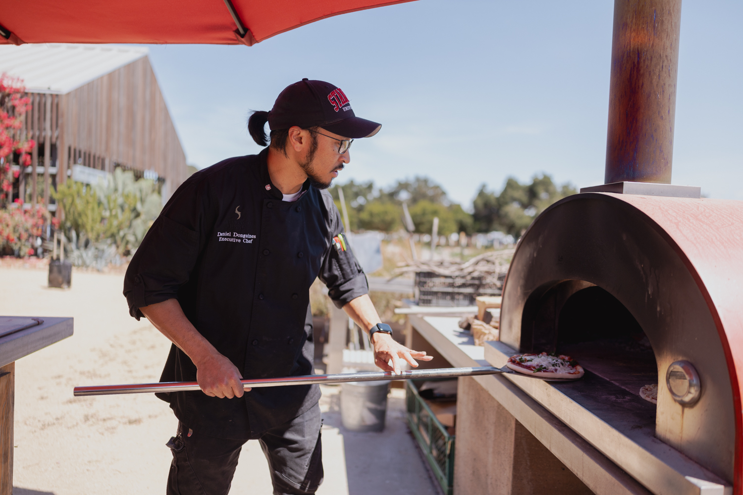 Image of Daniel Donguines demonstrating how to use the farm's outdoor pizza oven.