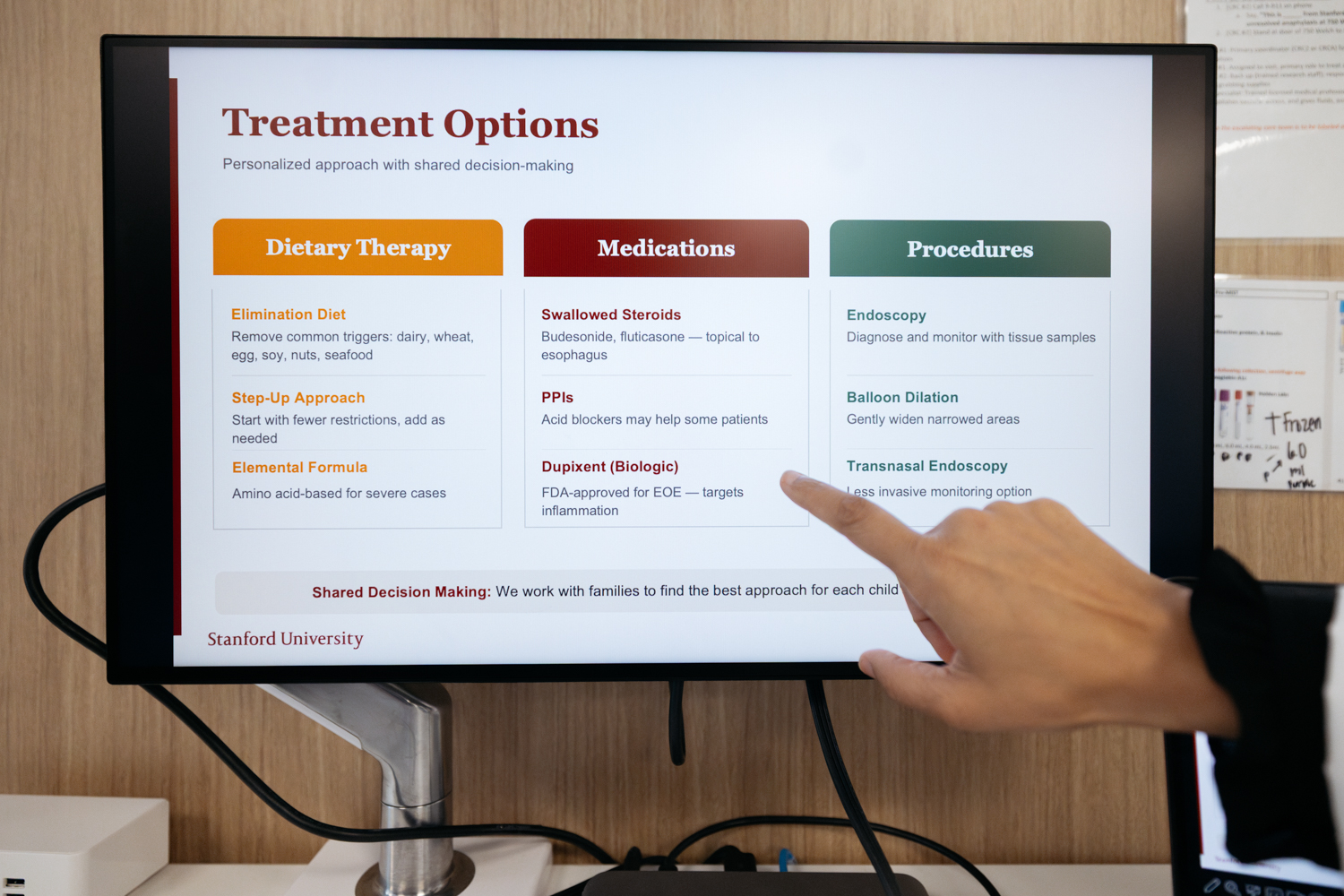 Computer screen displays treatment options for a medical condition, with a finger pointing at the information.