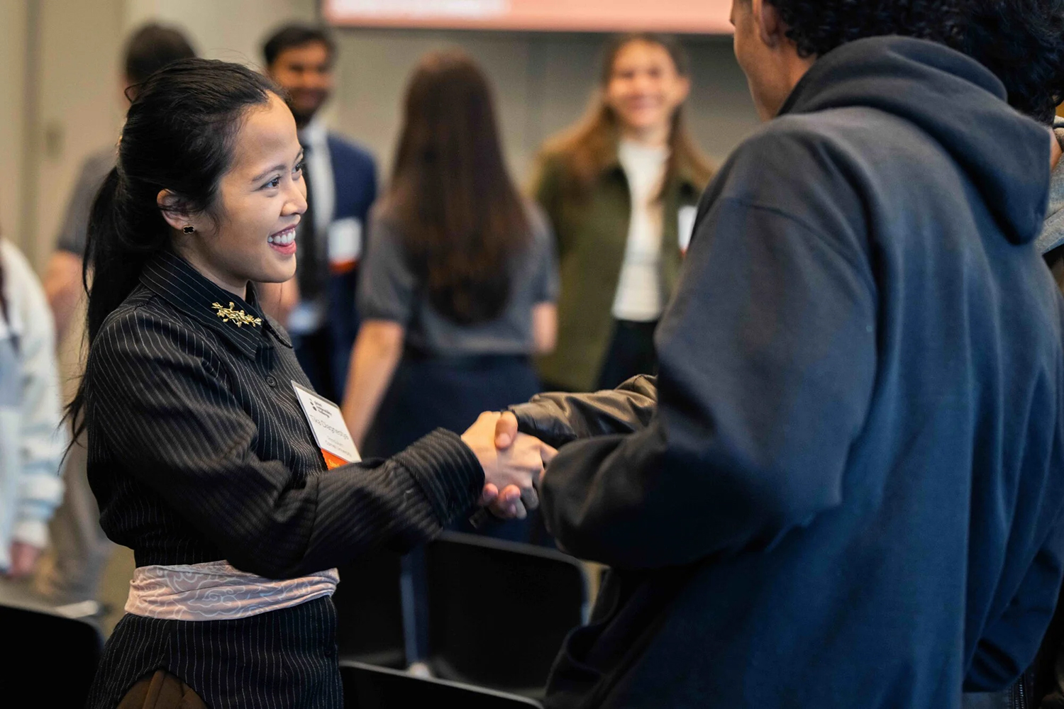 A person in formal attire shakes hands with another individual at a networking session.