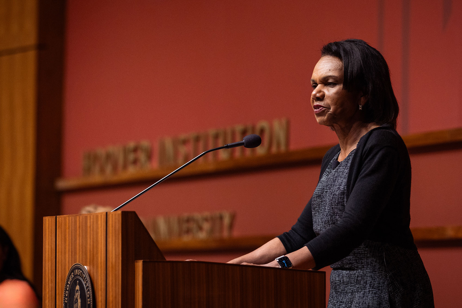 Condoleezza Rice standing behind a podium, speaking into a microphone during an event at the Hoover Institution.