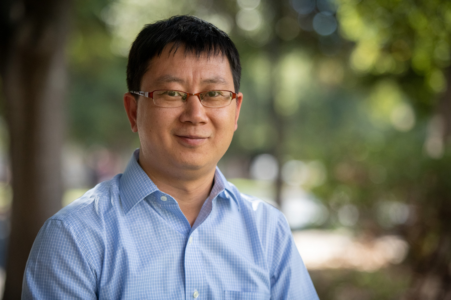 Xiaoke Chen wearing a light blue shirt posing for a photo outdoors with a blurred background.