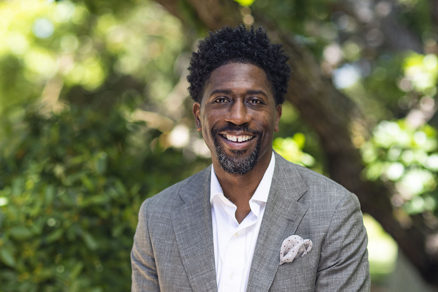 Lerone Martin smiling in a gray suit jacket outdoors with trees in the background.