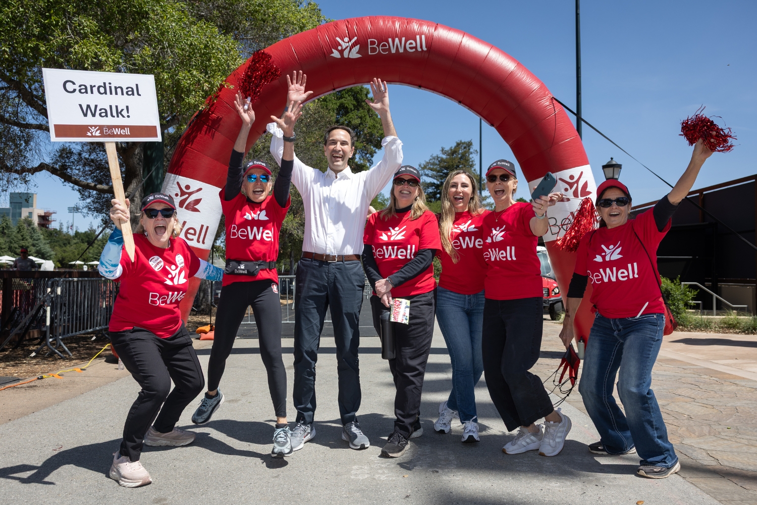 A group of enthusiastic participants pose with President Levin under a red arch, celebrating the 