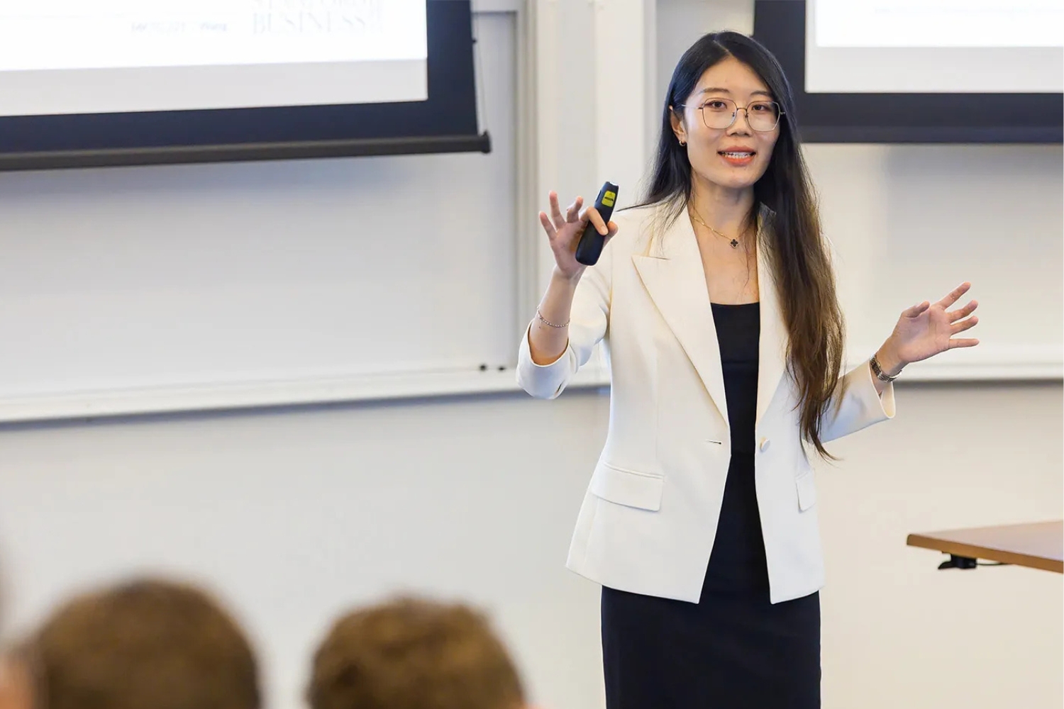 Yuyan Wang presents to an audience, holding a remote in one hand, in a classroom setting.