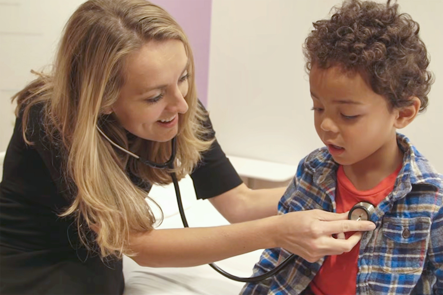 A doctor checks a child's heartbeat with a stethoscope in a medical office.