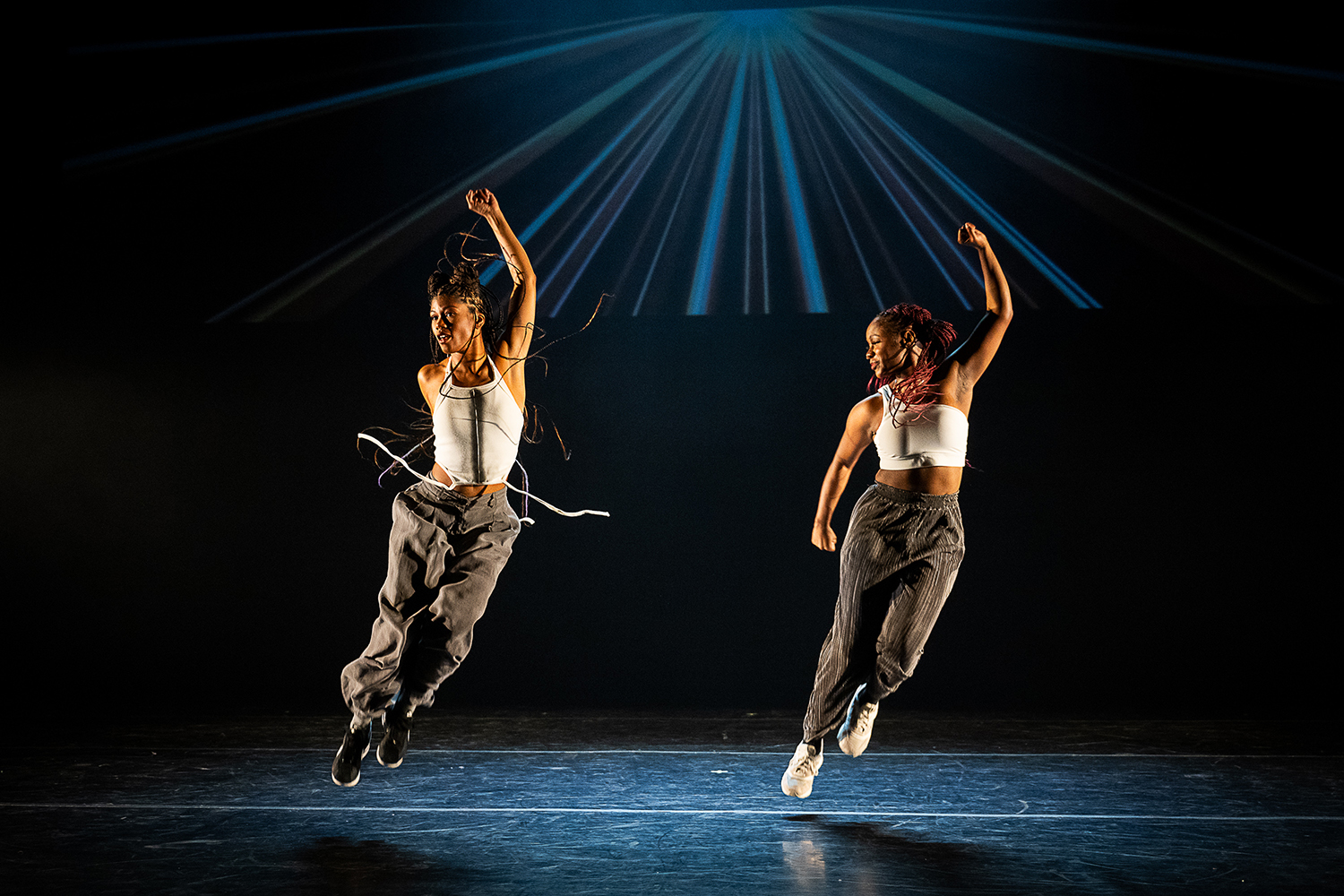 Two dancers leap into the air on stage, showcasing motion against a dramatic light backdrop.