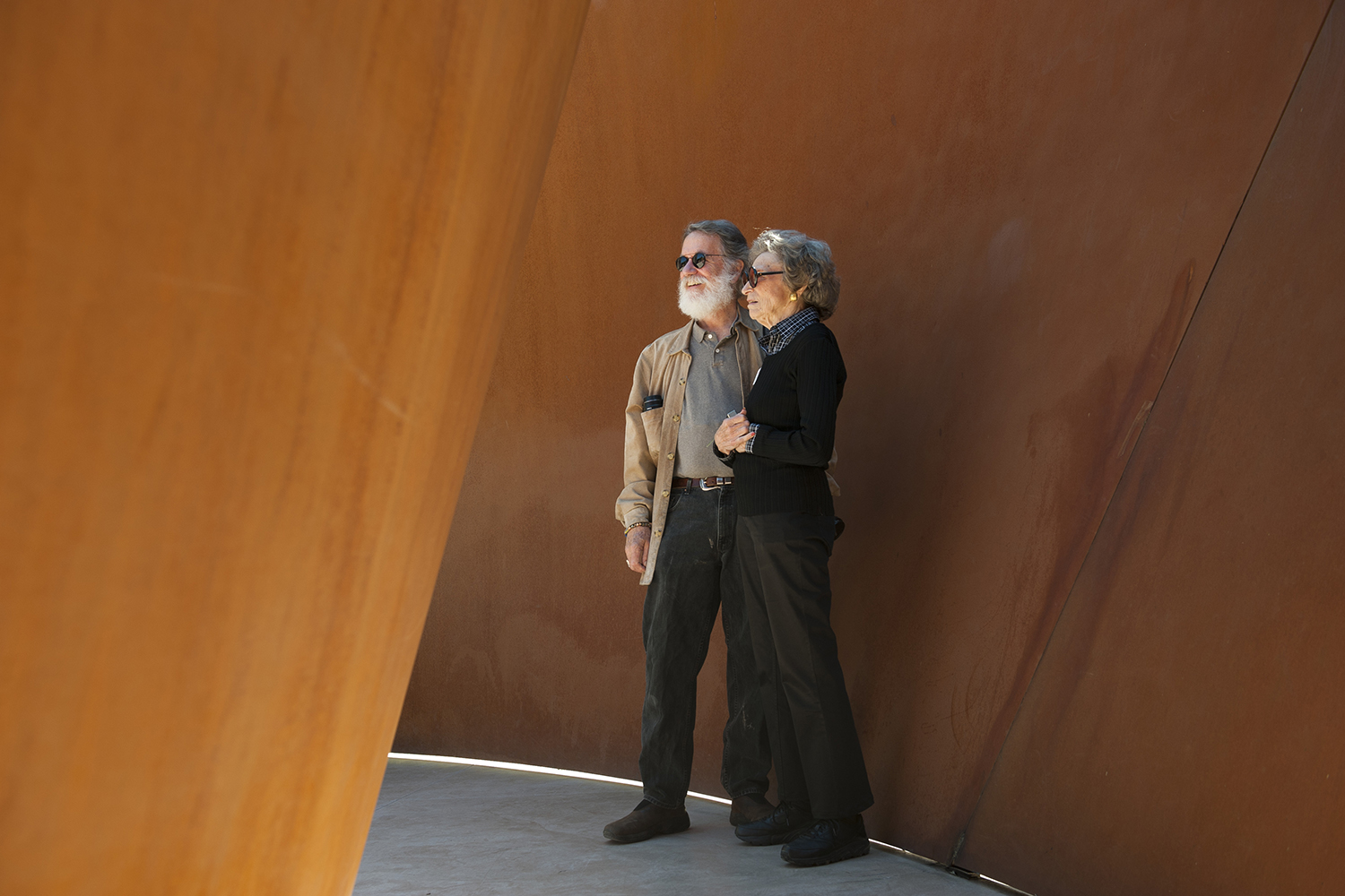 Seligman and Fisher stands together in a modern, rust-colored architectural space of sculpture Sequence.