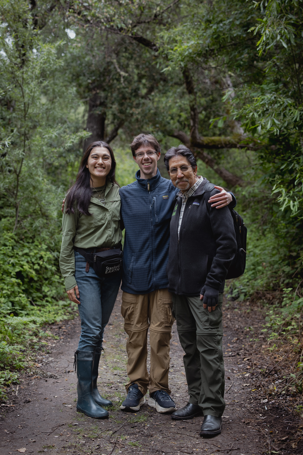 Course instructors wearing outdoor gear stand on a trail in a wooded area.