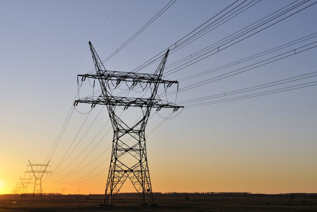 High-voltage power lines and a tower silhouetted against a sunset sky.