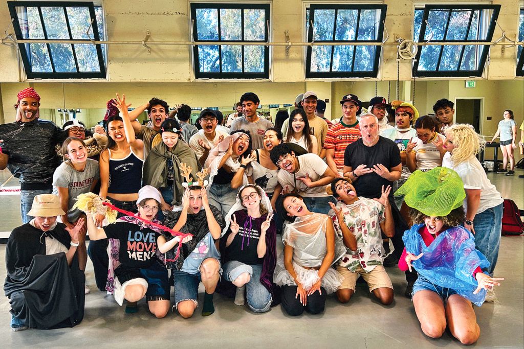 Dance group in colorful costumes poses enthusiastically in a rehearsal studio.