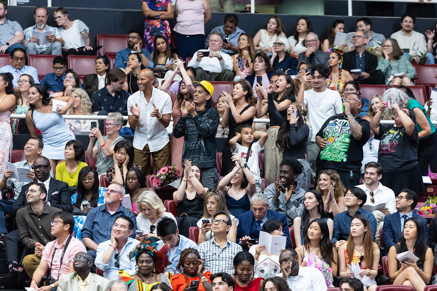 Audience members stand and applaud while some record the ceremony on their phones.