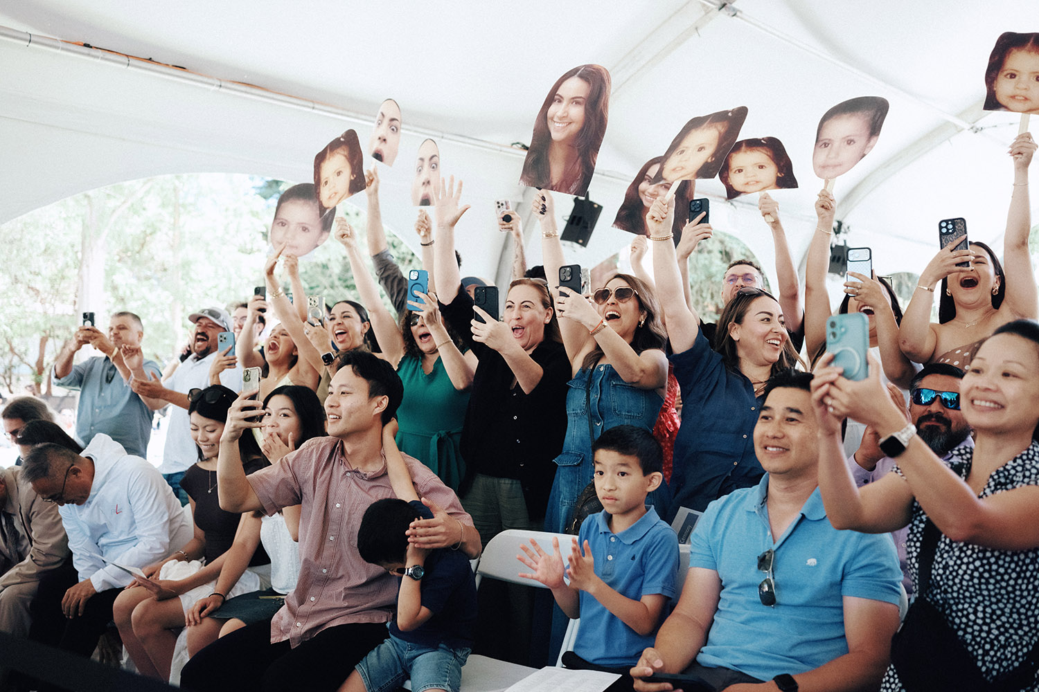 A crowd of excited audience members holds up cell phones and cardboard cutouts of faces during the event.