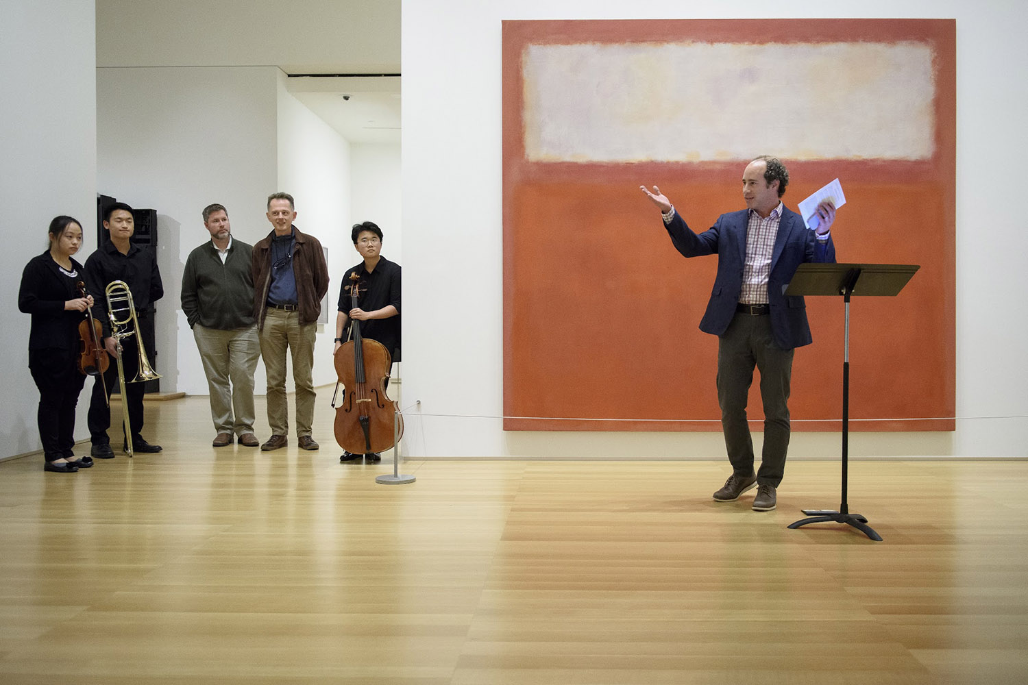 Linetzky gestures while speaking to an audience, with musicians standing nearby in an art gallery setting.