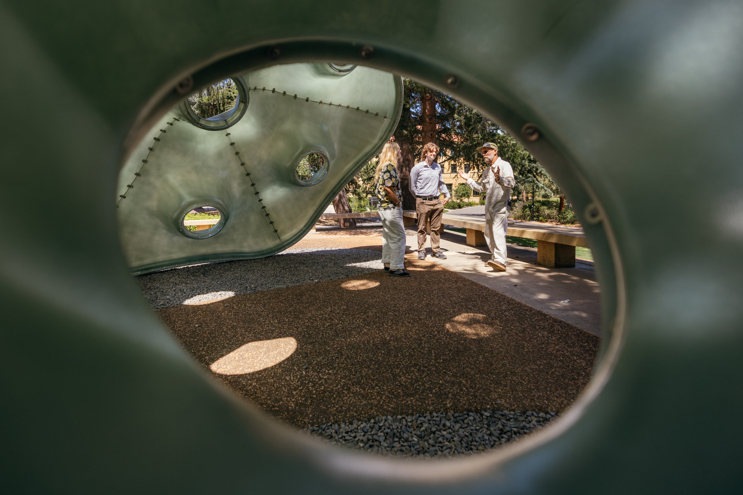 A view through an opening in a green sculpture showing an art ranger talking with two visitors beside the artwork.