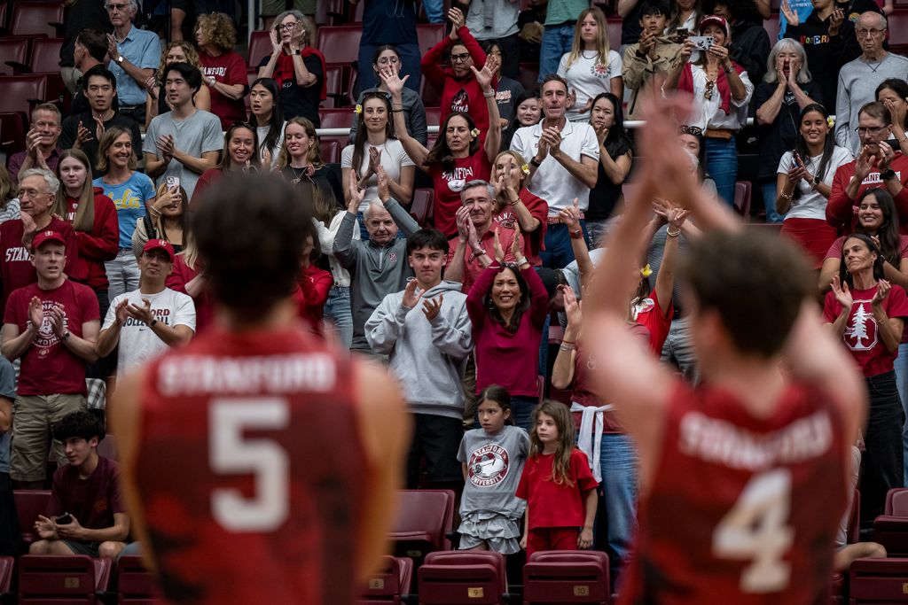 Fans cheer and applaud from the stands as Stanford athletes face the crowd during a home game.