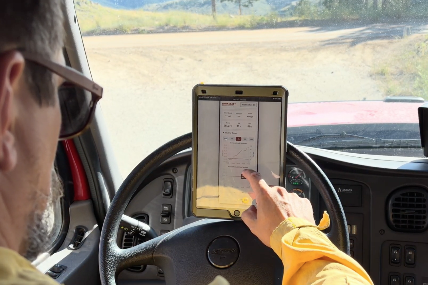 Firefighter in a truck cab points at a tablet displaying SmokeCast fire weather data and charts.