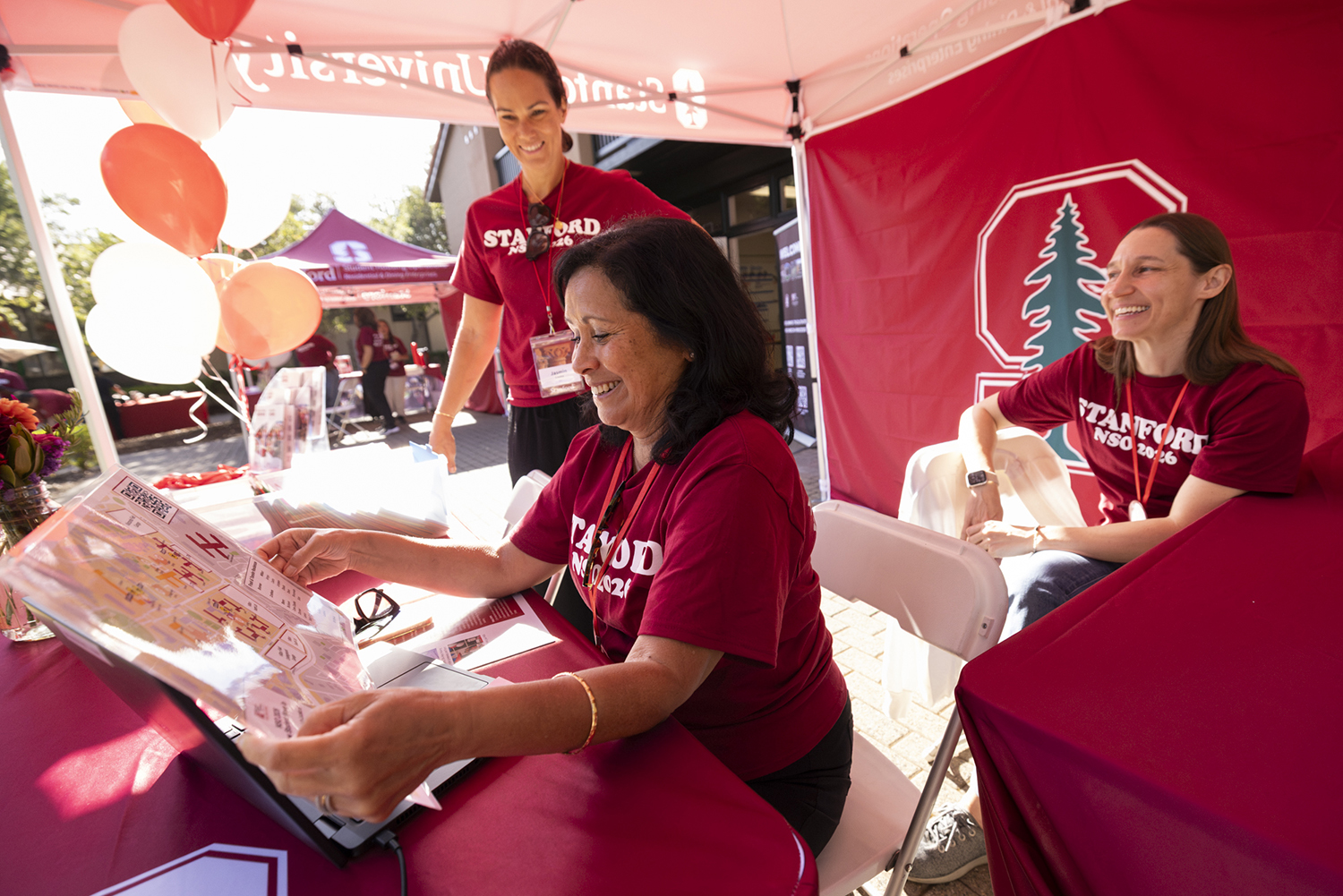 Orientation volunteers wearing matching shirts help a new student navigate a campus map at a welcome tent.