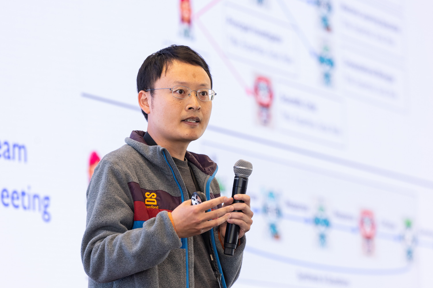 James Zou holding a microphone and gesturing while speaking at an event.