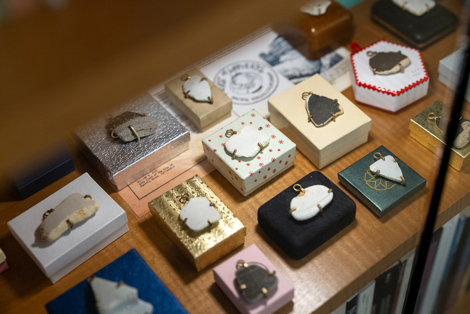 Ceramic shards in metal settings sit on small gift boxes in a display case with archival papers.