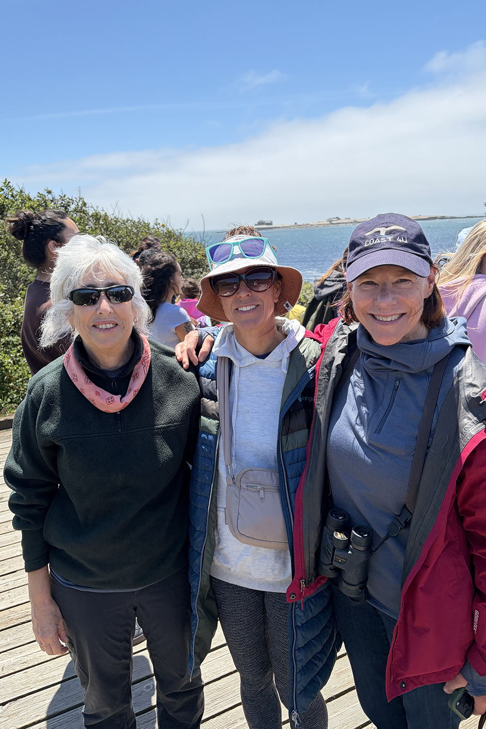 Deborah Sivas, Alexandria Boehm, and Meg Caldwell stand on a coastal boardwalk, with ocean and blue sky behind.