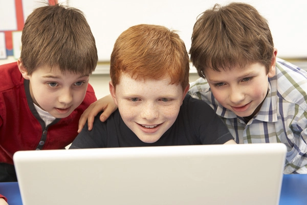 Three school-age boys looking at a laptop computer