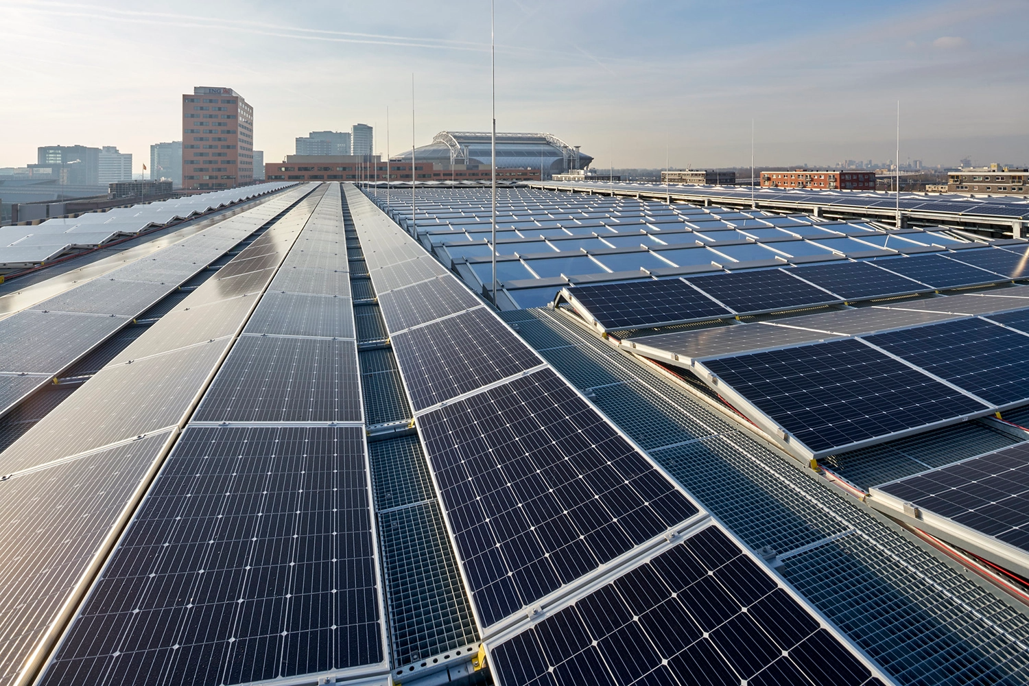 Solar panels installed on a flat rooftop, with the skyline of a city in the background under a clear blue sky.
