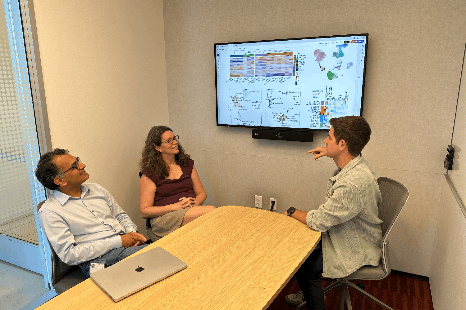 Image of Purvesh Khatri, Angela Rogers and Andrew Moore sitting in a small meeting room and discussing a new scoring system that indicates the status of a patient's immune system health.