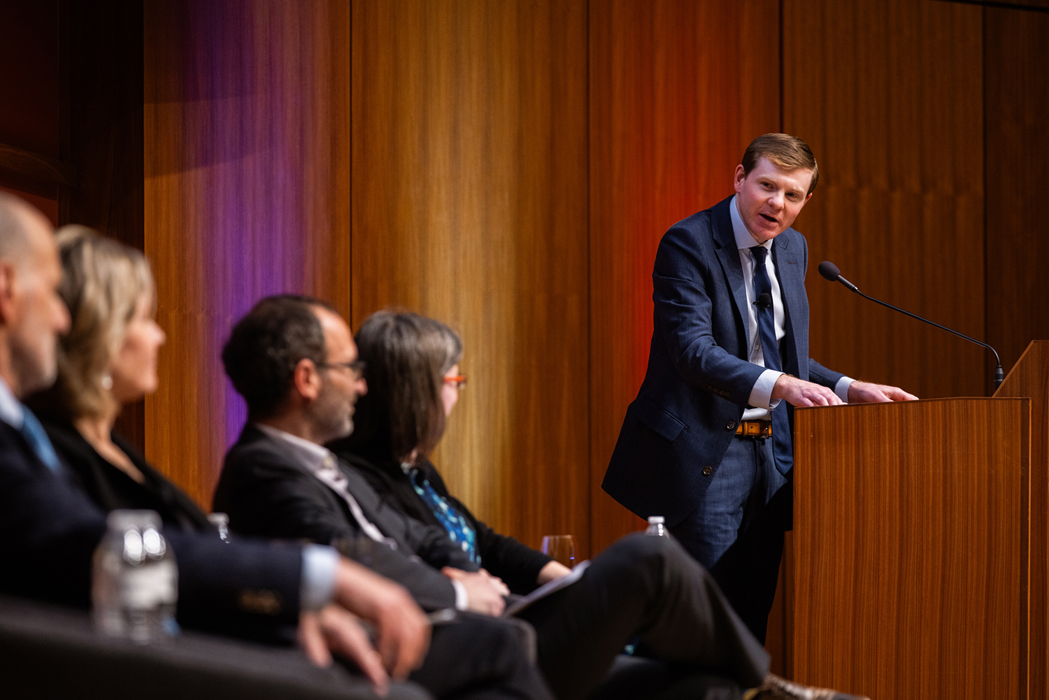 Jonathan Gienapp presenting at a panel discussion, with seated participants and an audience in a modern auditorium setting.