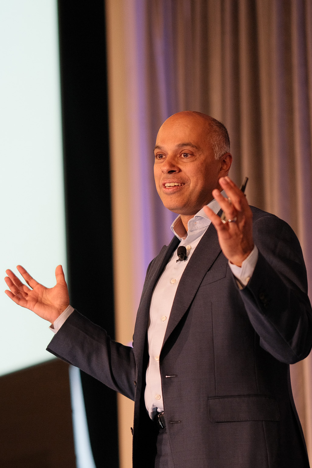 Amit Sevak gestures with hands while addressing an audience, emphasizing points during a presentation on stage.