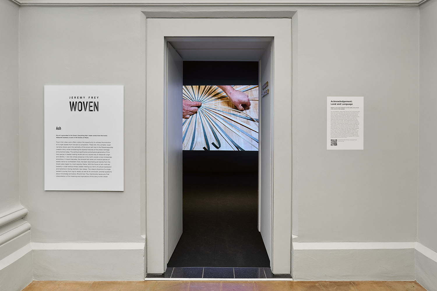 Gallery entrance with exhibition panels and a view of hands weaving a basket.
