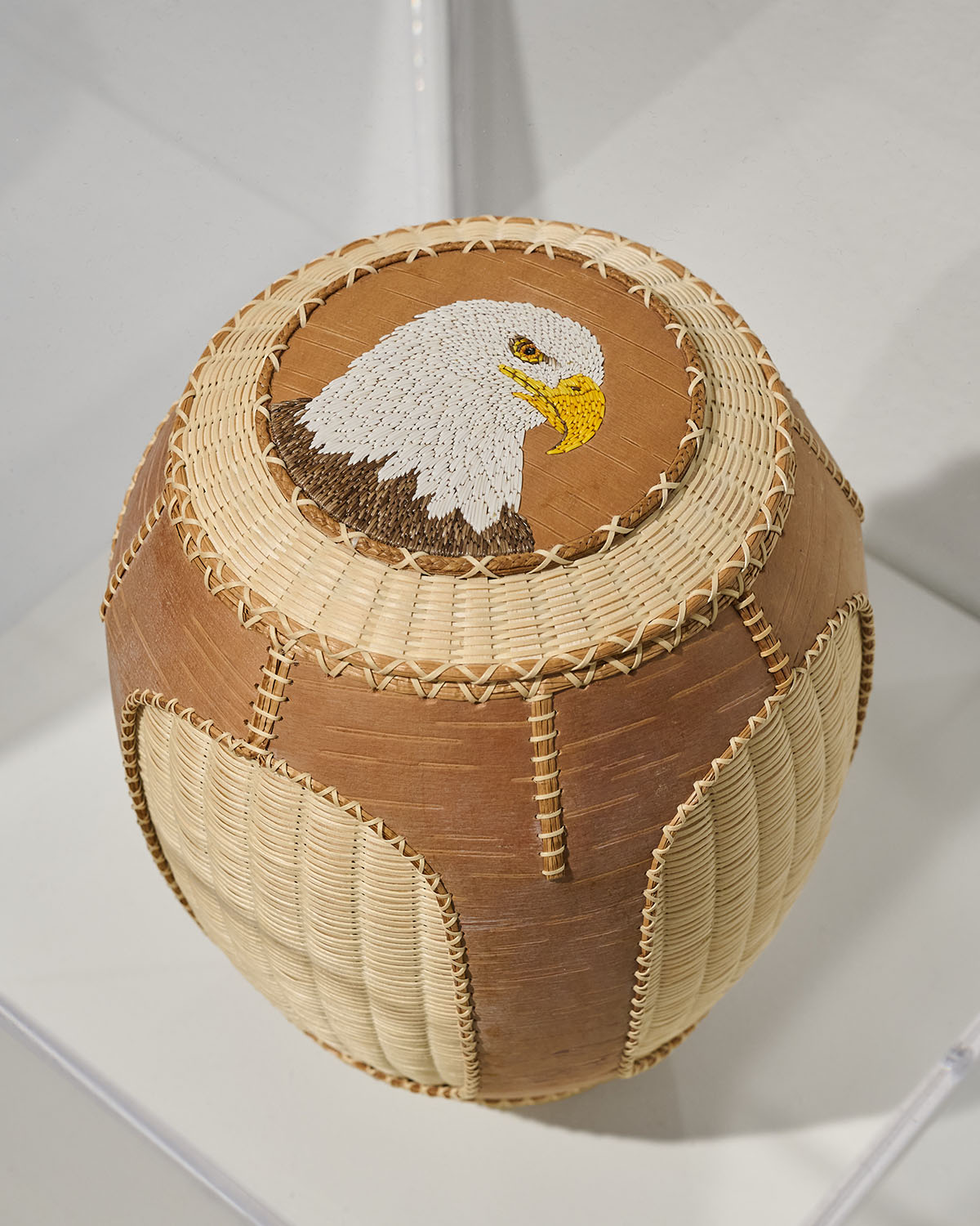 Woven basket in natural brown and cream tones with lid featuring detailed eagle head design.