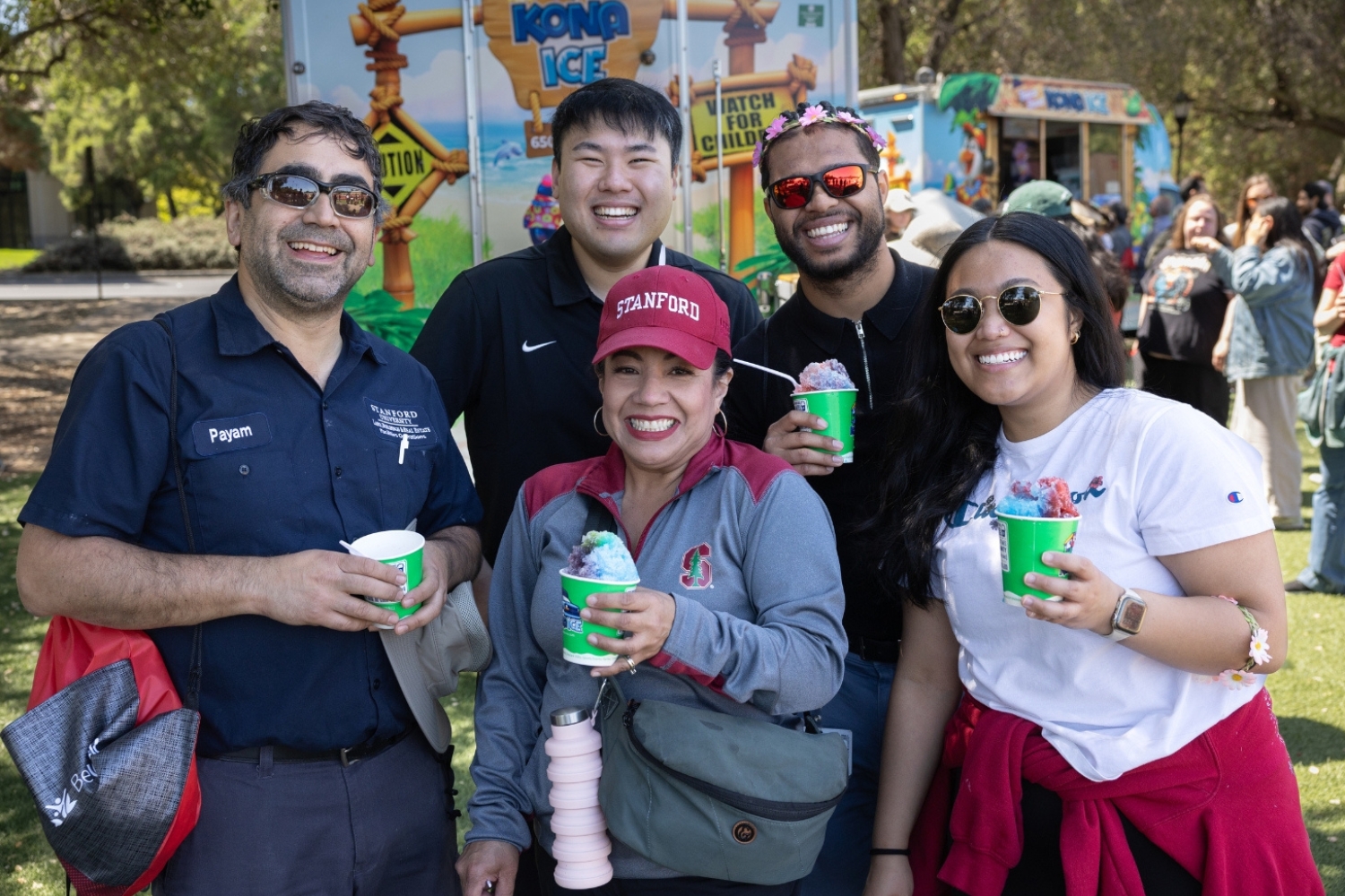 A group of people posing with colorful frozen treats in cups, enjoying a day at an outdoor event.