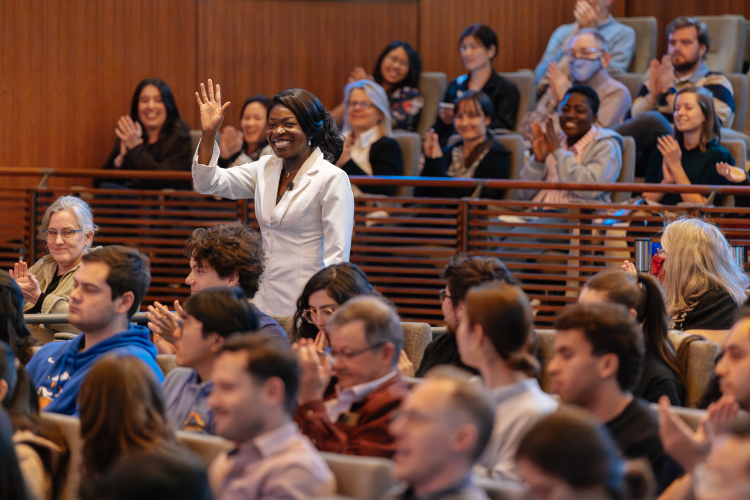 Ibukun Ajifolokun in white blazer standing and waving in auditorium as audience applauds.