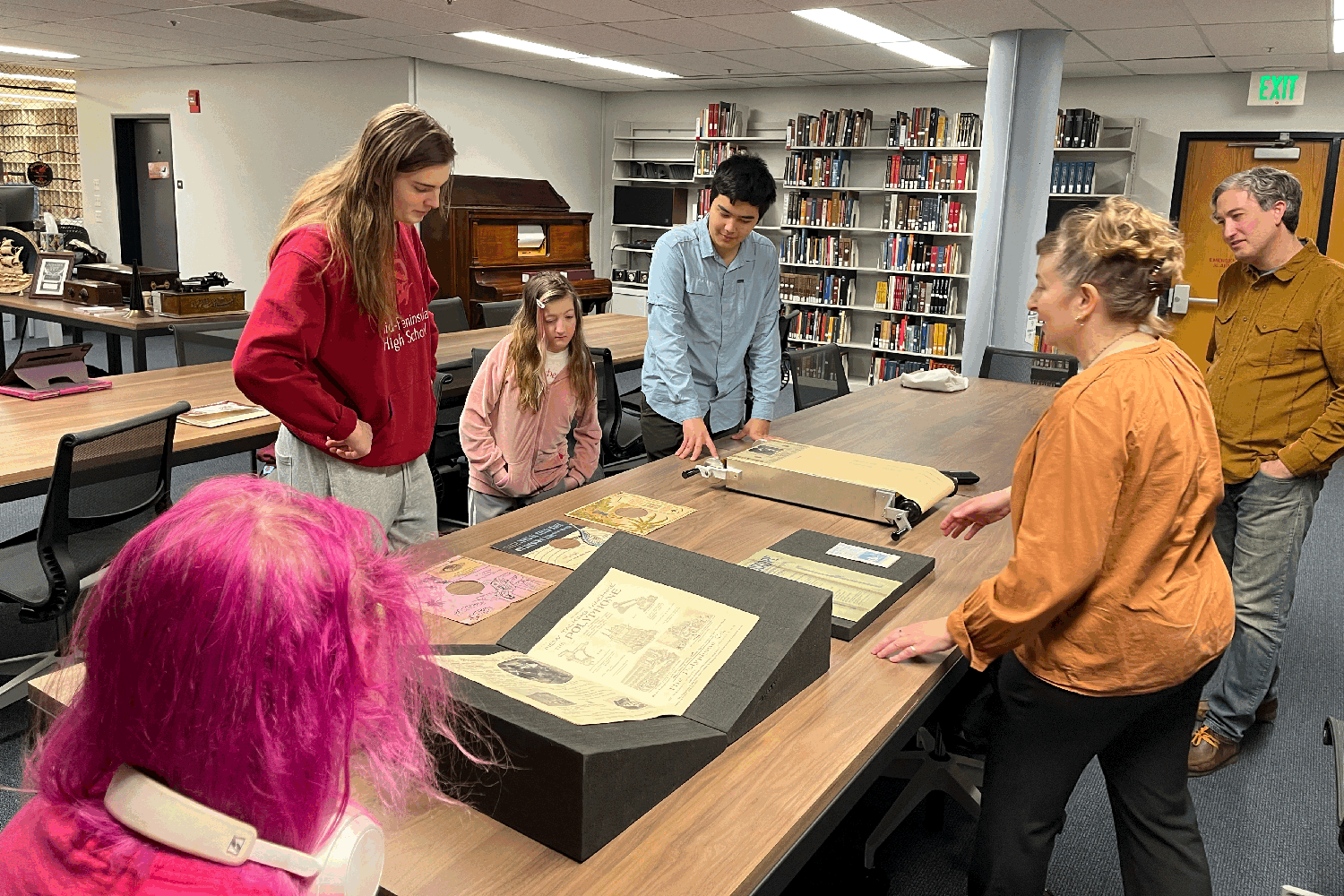 Students examine historical documents displayed on a table in a library.