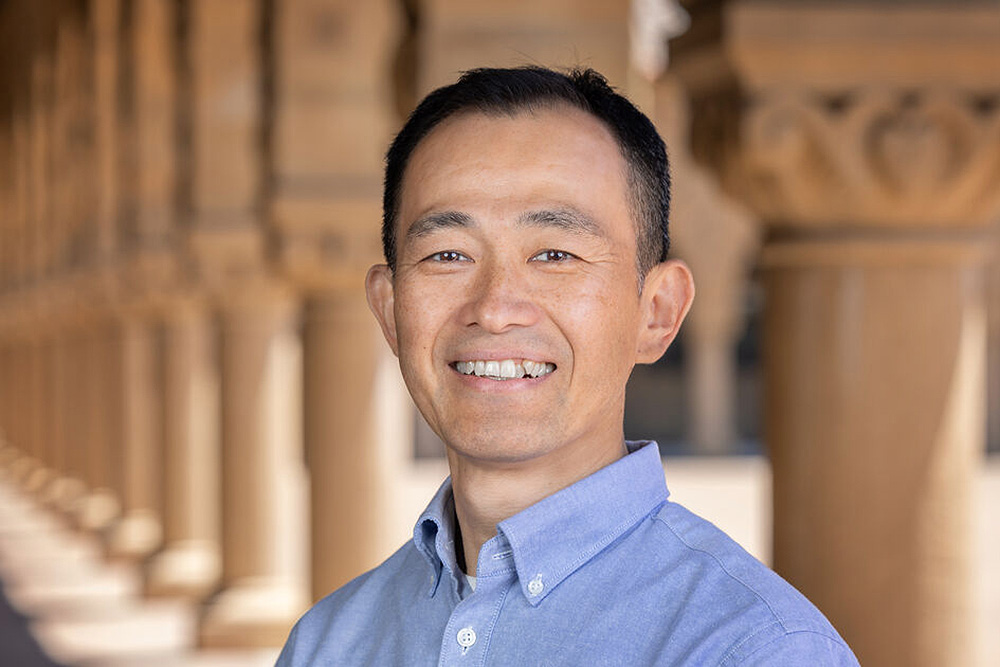 Tadashi Fukami in a blue shirt stands in front of a stone colonnade.