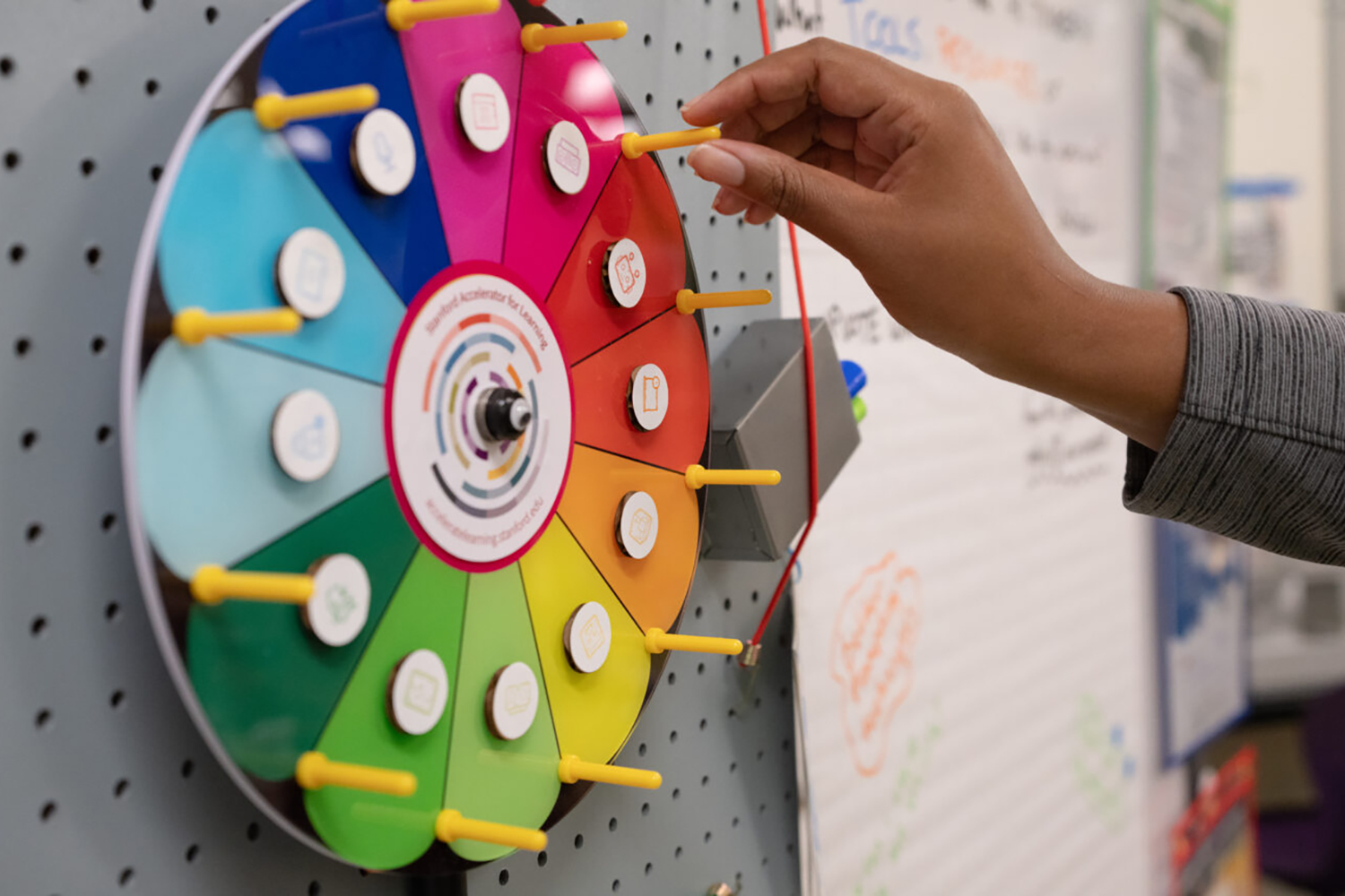 A hand is spinning a colorful wheel with icons, used for decision-making in a classroom setting.