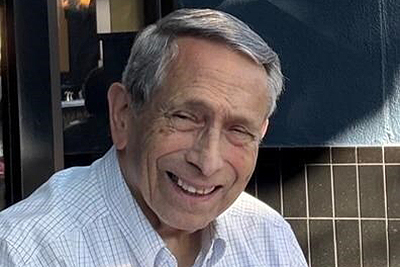Snapshot of Ronald Castellino with gray and wearing a light-colored plaid shirt, in a casual outdoor setting.