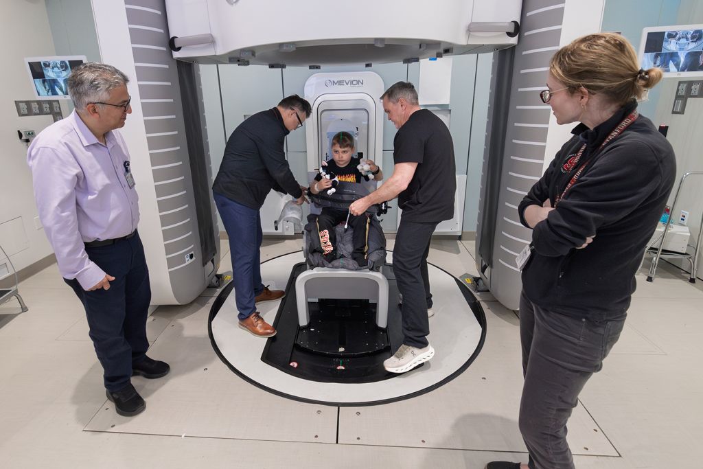 A child sits in a medical machine while adults assist, preparing for a procedure in a healthcare setting.