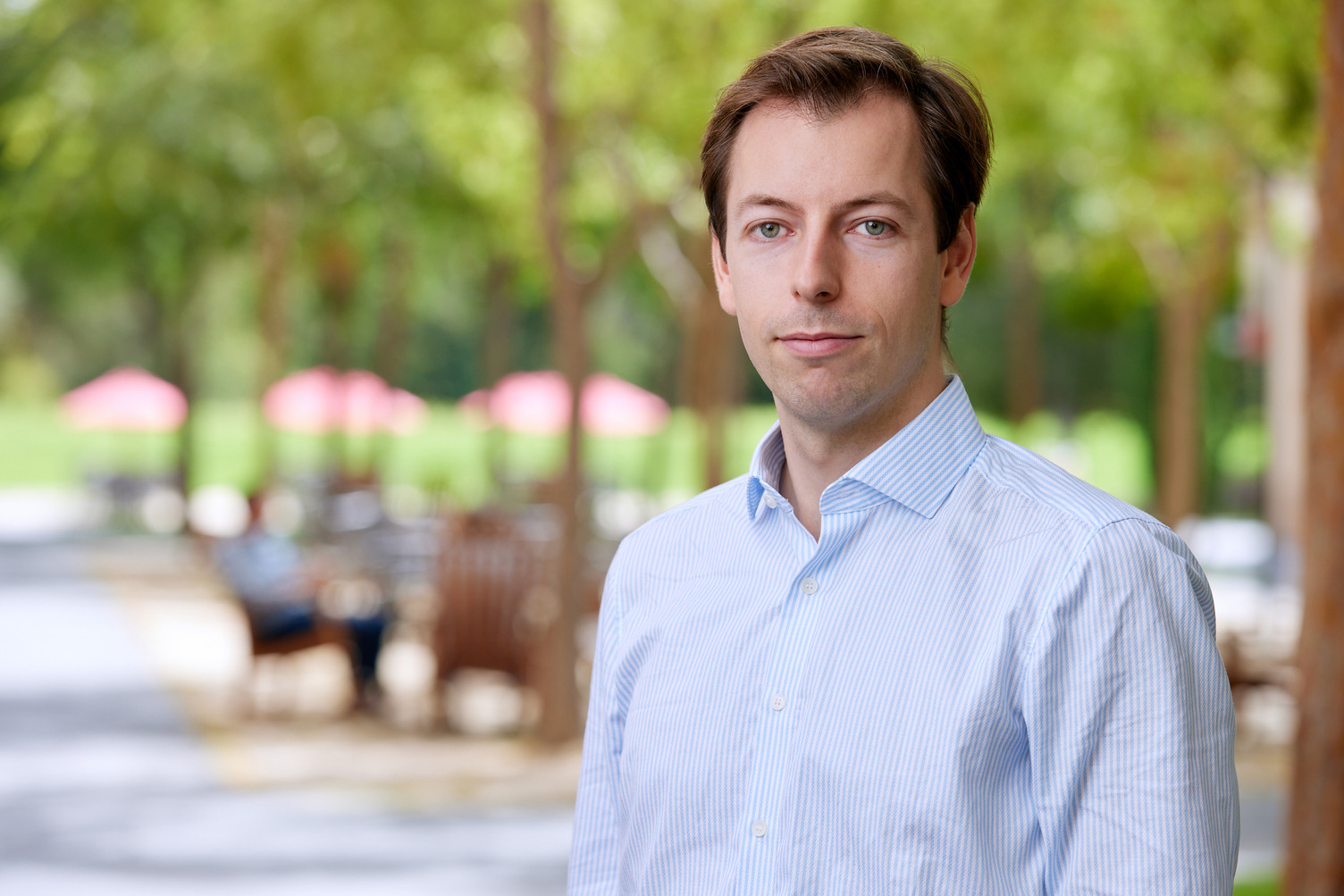 Fabian Nagel stands outdoors with blurred figures and trees in the background.